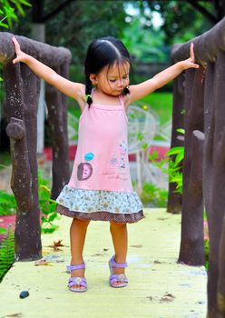A little girl standing on a bridge with arms spread wide open.