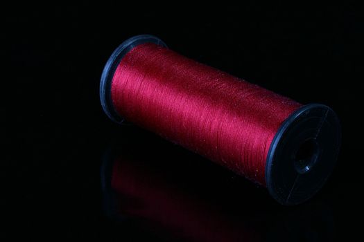 Darkly red threads on the coil for industrial use. Threads are placed on a black reflecting background.