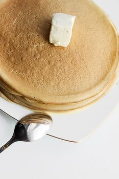 Pile of pancakes with butter and spon on plate