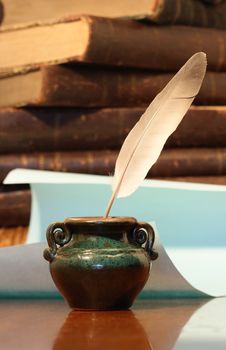 Still life with old inkpot with feather on vintage background with books