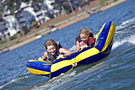 Young boy and girl on a tube behind a boat.