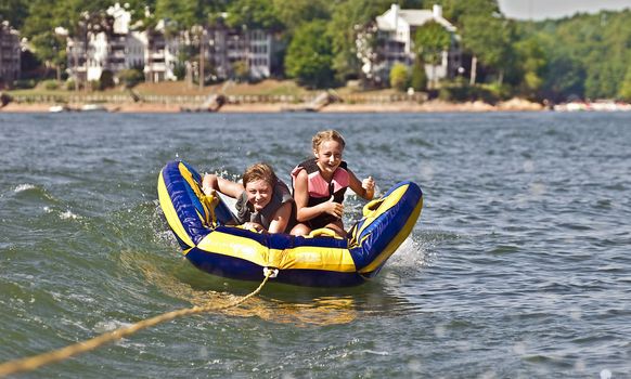 A young boy and girl riding a tube behind a boat.