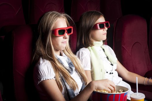 two girls look three-dimensional cinema, sitting in the glasses, eat popcorn, drink drink