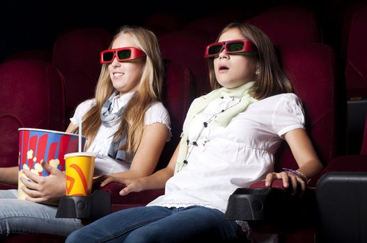 two girls look three-dimensional cinema, sitting in the glasses, eat popcorn, drink drink