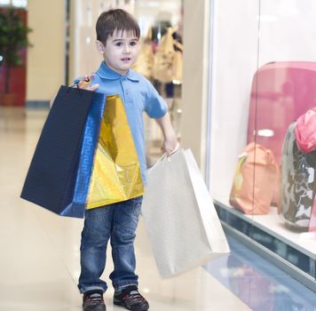 The child bears packages with purchases in shopping center