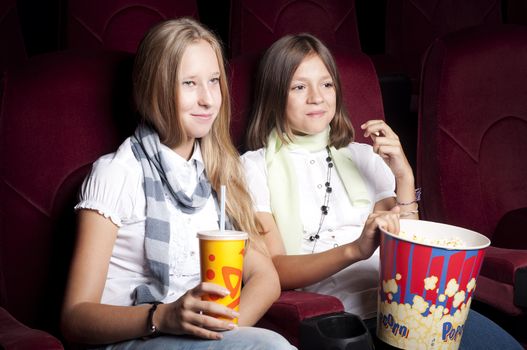 two girls look three-dimensional cinema, sitting in the glasses, eat popcorn, drink drink