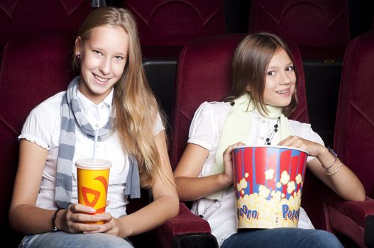 two girls look three-dimensional cinema, sitting in the glasses, eat popcorn, drink drink