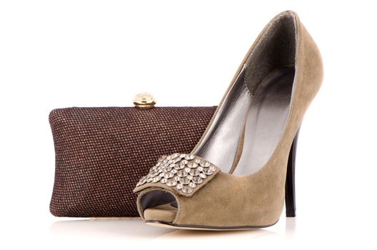 Female shoe and handbag on a white reflective background.