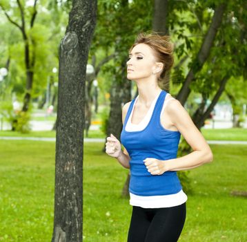 young woman jogging in the park in summer, trees and grass background