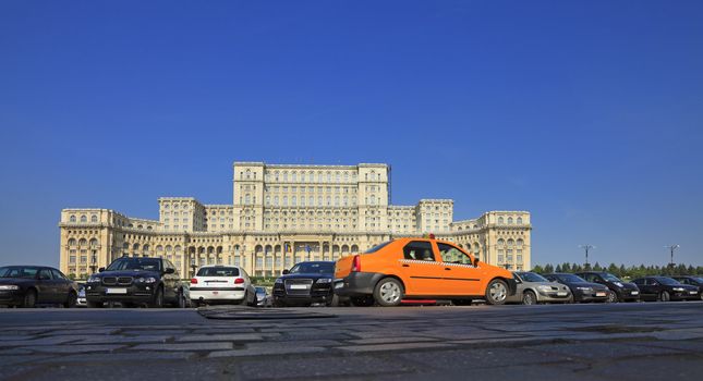 Yellow cab in front of the Parliament House in Bucharest,Romania.The main focus is on the building,the taxi presents some motion blur.