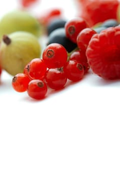 Spilled  mixed berries on white background whith a raspberry  in the foreground in focus.