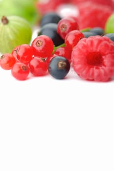 Spilled  mixed berries on white background whith a raspberry  in the foreground in focus.