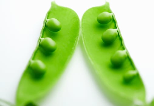  A close-up of a pea pod split open revealing peas on white background
