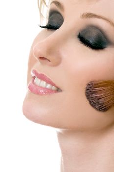 Female face and brush applying powder rouge to cheeks.
