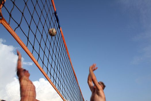 Men play beach volleyball, try to strike a ball in a jump