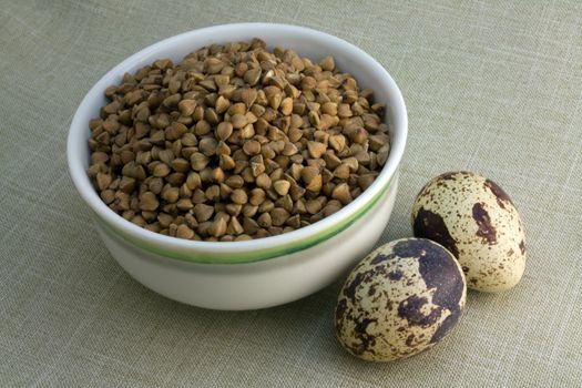 Small bowl of buckwheat and two quail eggs on linen background