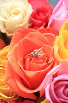 A wedding band and a diamond solitaire in an orange rose in the middle of a mixed bouquet of roses