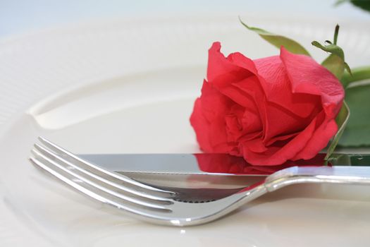 A fork and knife and a red rose, perfect for a dinner invitation