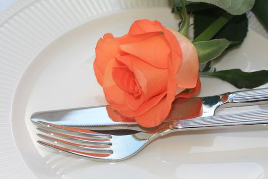 A fork and knife and an orange rose, perfect for a dinner invitation