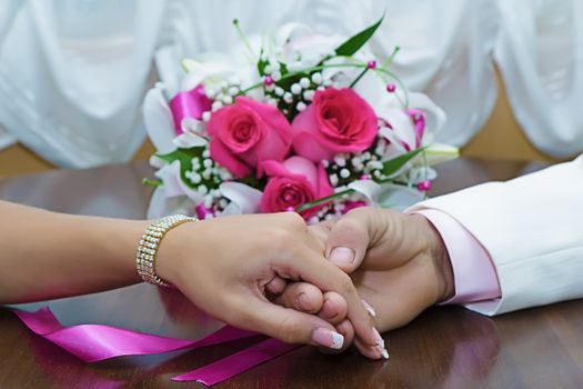the hands of the newlyweds and bridal bouquet on the table