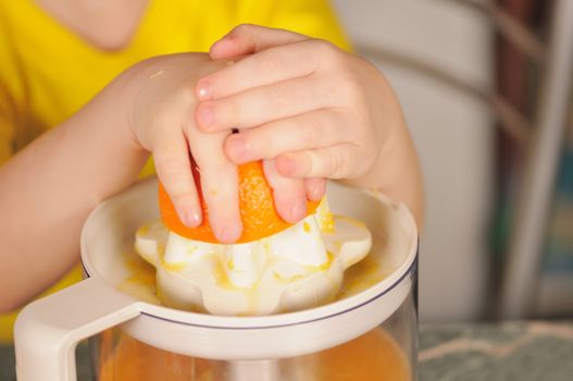 The child in a yellow vest to wring out juice  from an orange