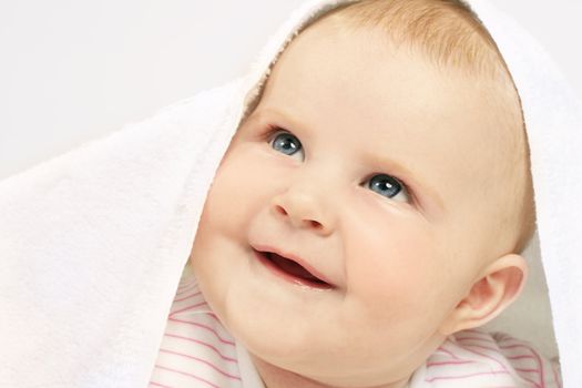 Adorable baby under a towel, looking up and smiling.