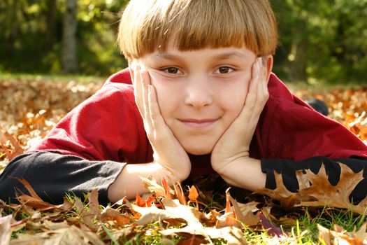 A boy laying in a park with his head in both hands and staring ahead.