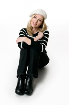 Relaxed casual woman wearing black jeans, black leather boots and black and white sweater sitting on a white background.