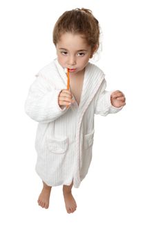 A small toddler girl in bathrobe is standing and brushing her teeth