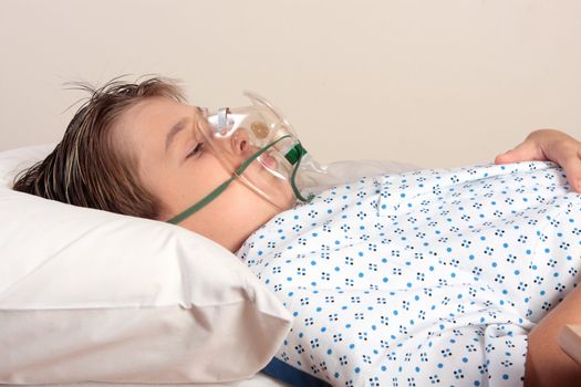 A child resting on a bed wearing patient gown has an oxygen mask or inhaler over face.