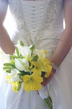 A young bride holds her flower bouquet behind her back.