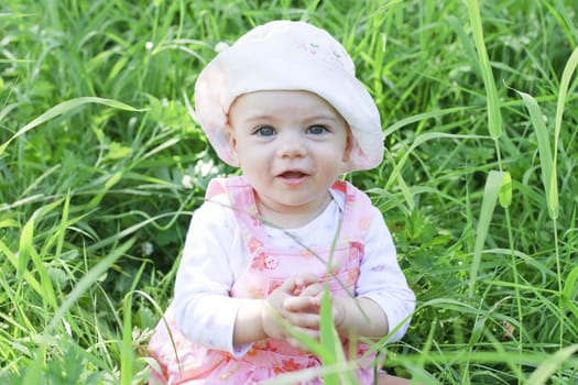 Happy baby girl with blue eyes lying on grass