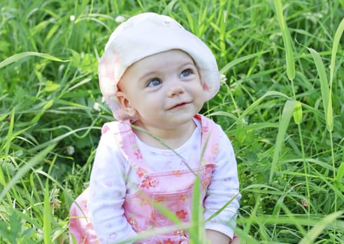 Happy baby girl with blue eyes lying on grass