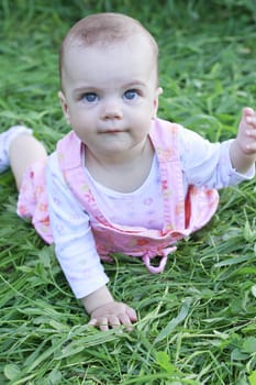 Happy baby girl lying on grass with her hand at camera