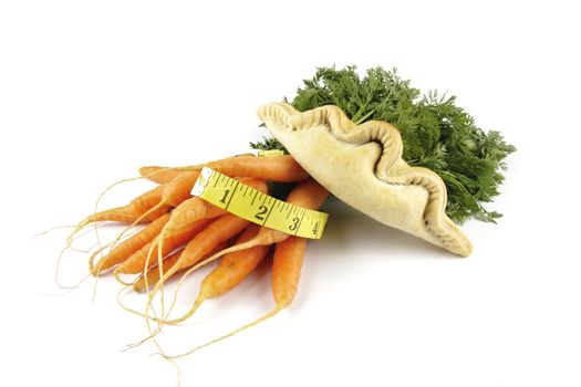 Contradiction between healthy food and junk food using bunch of carrots and pasty with a tape measure on a reflective white background 