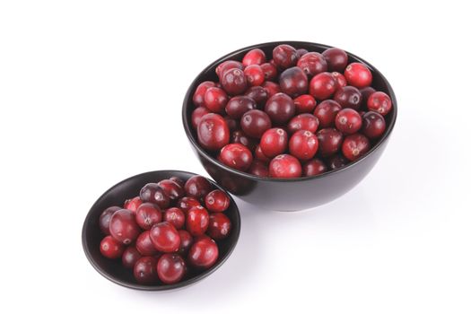 Red ripe cranberries in a small round black bowl and a larger black bowl with a reflective white background