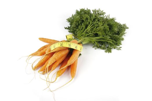 Fresh young bunch of carrots with green leafy stems and tape measure on a reflective white background