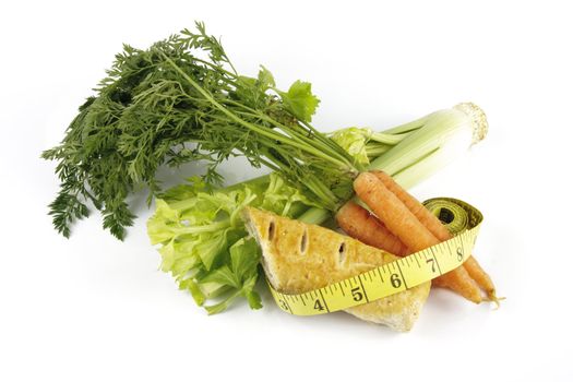 Contradiction between healthy food and junk food using a bunch of carrots and sausage roll with a tape measure on a reflective white background 