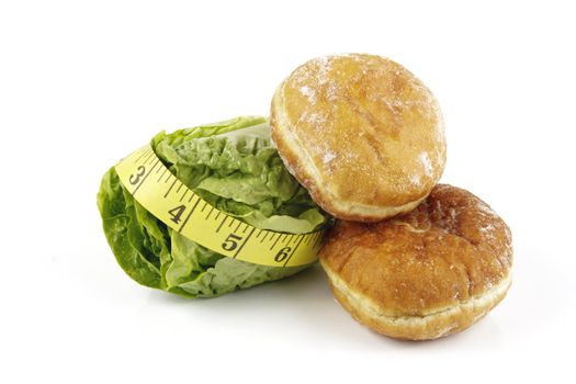 Contradiction between healthy food and junk food using a green salad lettace and jam doughnut with a yellow tape measure on a reflective white background 