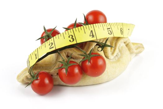 Contradiction between healthy food and junk food using tomatoes and a pasty with a tape measure on a reflective white background 