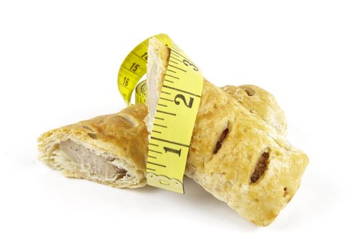 Single golden sausage roll cut in half with yellow tape measure on a reflective white background