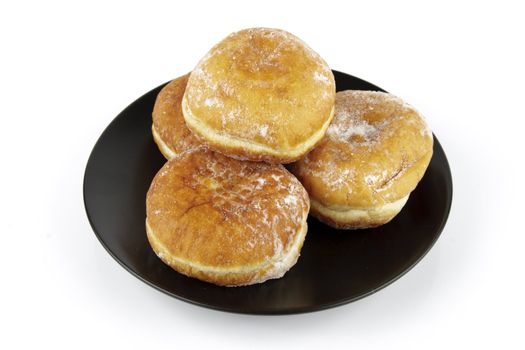 Black round plate of jam doughnuts on a reflective white background