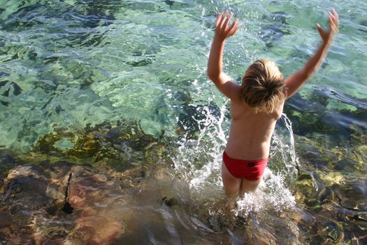 Boy splashes water overhead from an ocean rockpool.   
Somet motion blur in the hands.
