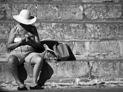 Female tourist sitting on steps in Mdina in Malta checking her mobile phone