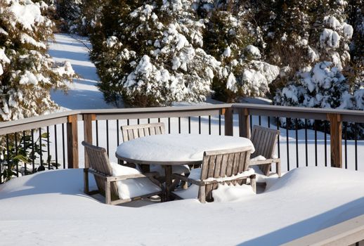 Two tier deck covered with deep snow covering a small wooden table and chairs