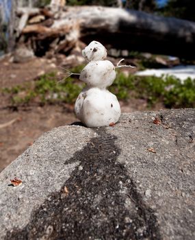 Small snowman on granite rock is melting in the warm sunshine