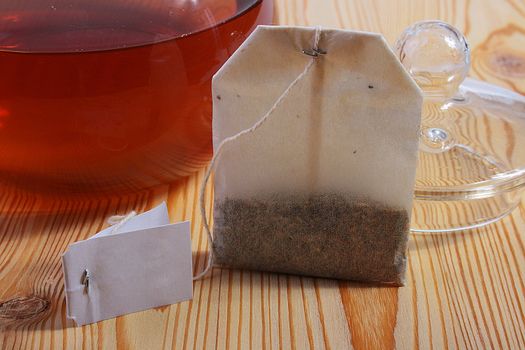 Tea in a paper bag against a wooden table and a glass teapot for tea leaves.