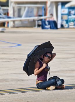 LUQA, MALTA - SEP 26 - A female spectator shades herself from the hot sun and sits down on the tarmac during the Malta International Airshow 26th September 2009