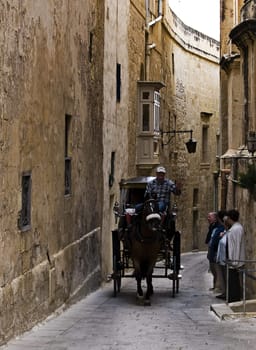 MDINA, MALTA - DEC 27 - A traditional Malta horse-drawn carriage known locally as Karrozzin passes through the street of Mdina