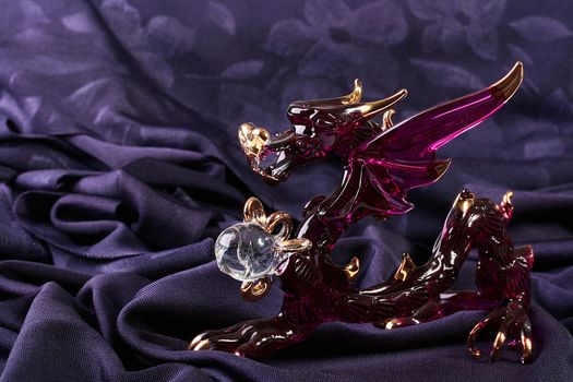 Glass figure of darkly red dragon on darkly violet fabric.